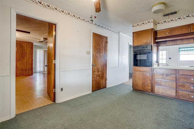 kitchen with wood walls, a textured ceiling, dark carpet, black oven, and ceiling fan