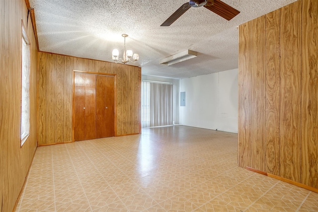 unfurnished room featuring ceiling fan with notable chandelier, electric panel, a textured ceiling, and wood walls