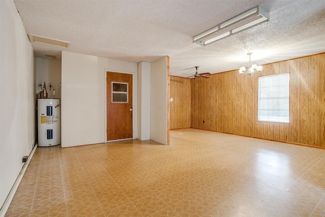 empty room featuring water heater, ceiling fan with notable chandelier, a textured ceiling, and wood walls