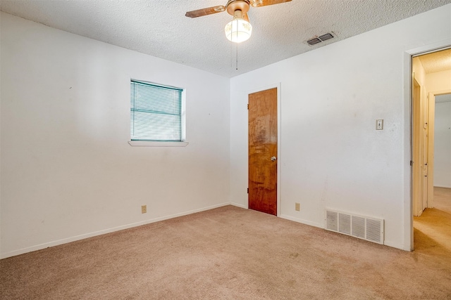 empty room with ceiling fan, light colored carpet, and a textured ceiling