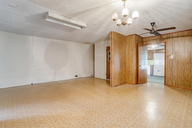 spare room with ceiling fan with notable chandelier, a textured ceiling, and wood walls