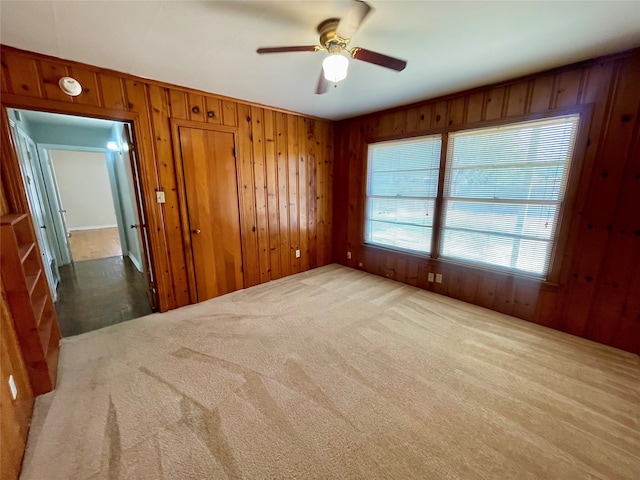 carpeted spare room with wood walls and ceiling fan