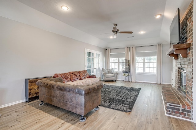 living room with brick wall, ceiling fan, light wood-type flooring, and a brick fireplace