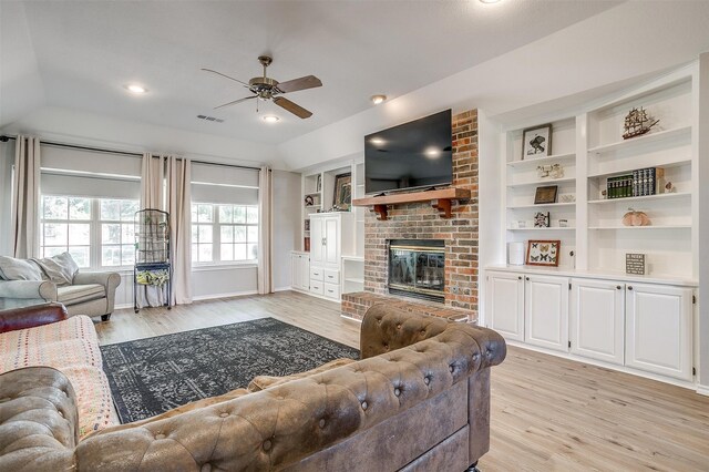 living room with ceiling fan, a fireplace, light hardwood / wood-style flooring, and brick wall