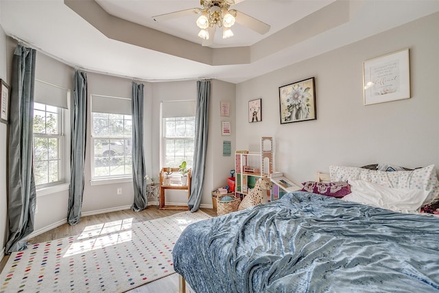 bedroom with multiple windows, light wood-type flooring, a tray ceiling, and ceiling fan