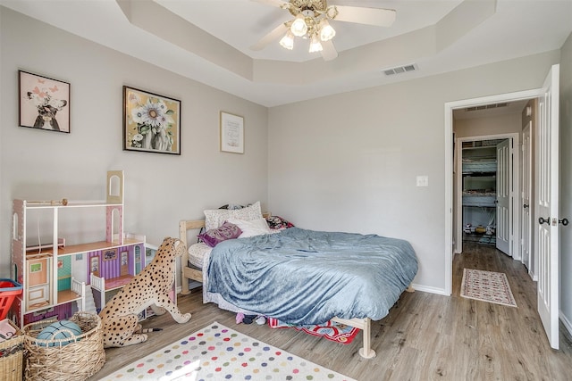 bedroom featuring ceiling fan, light wood-type flooring, and a tray ceiling