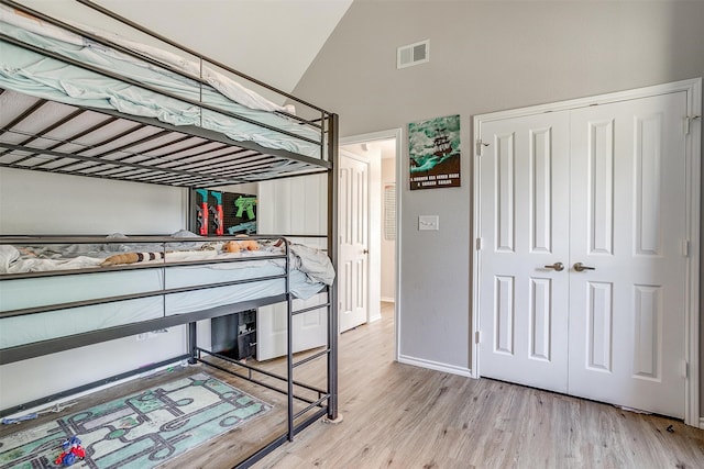 bedroom with light hardwood / wood-style floors, high vaulted ceiling, and a closet