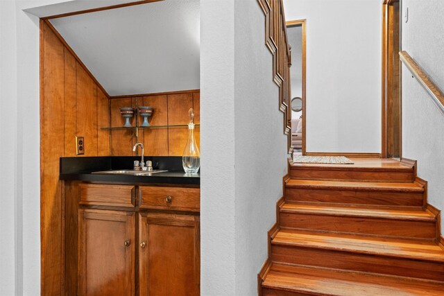 stairway with sink, wooden walls, and vaulted ceiling