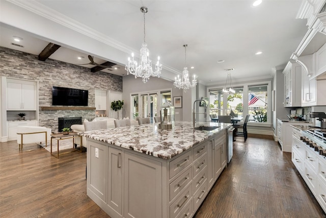 kitchen with an island with sink, dark wood-style flooring, beam ceiling, a fireplace, and a sink