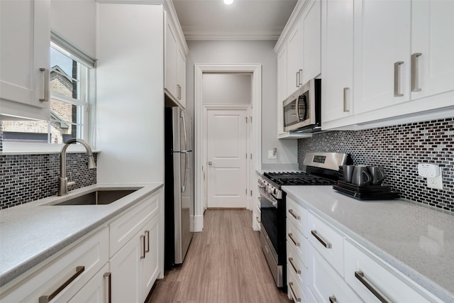 kitchen featuring stainless steel appliances, a sink, light wood-style floors, white cabinets, and tasteful backsplash