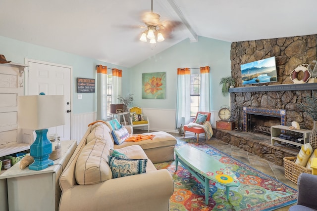 living room featuring a wealth of natural light, ceiling fan, vaulted ceiling with beams, and a stone fireplace