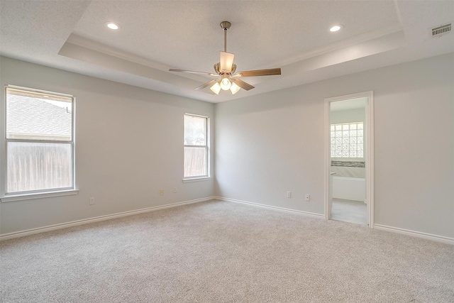 empty room with a wealth of natural light, a tray ceiling, visible vents, and baseboards