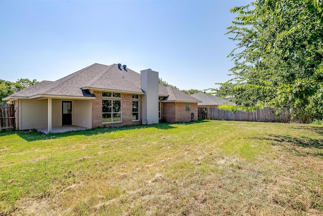 rear view of house featuring brick siding, fence, and a lawn