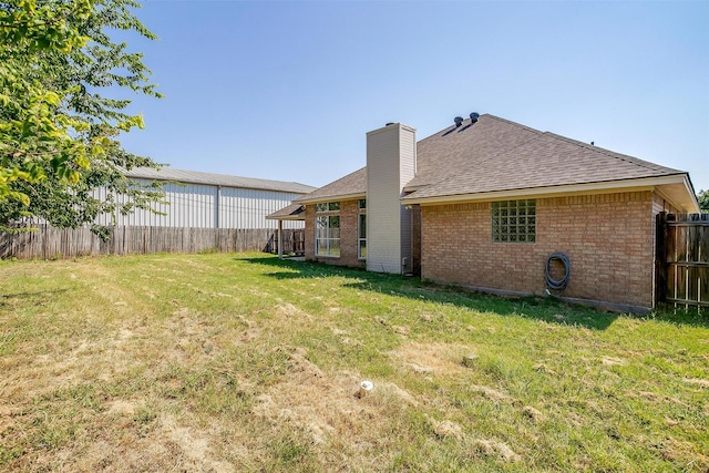 rear view of house with brick siding, fence, a yard, roof with shingles, and a chimney