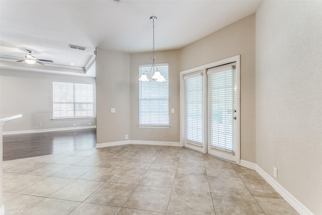 empty room featuring ceiling fan with notable chandelier, light tile patterned flooring, visible vents, and baseboards