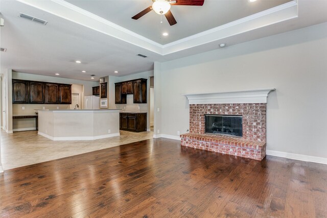 unfurnished living room with a raised ceiling, ceiling fan, light tile patterned flooring, and a brick fireplace