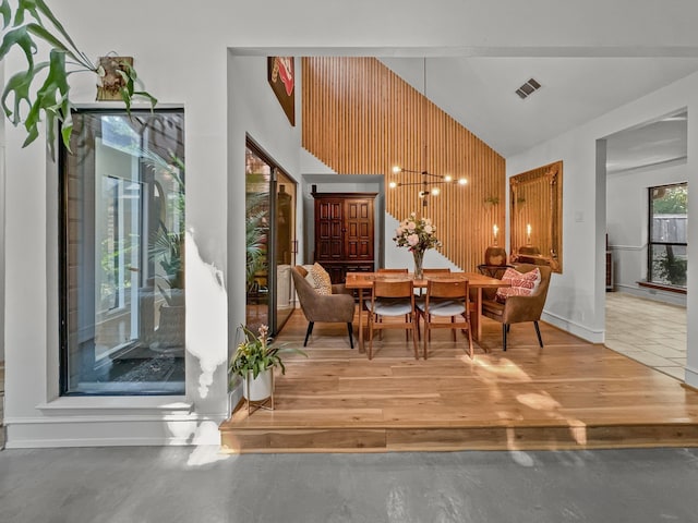 dining room with high vaulted ceiling, an inviting chandelier, and wood walls