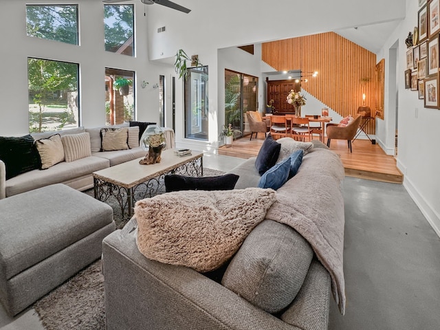 living room featuring a towering ceiling, ceiling fan, wooden walls, and concrete floors