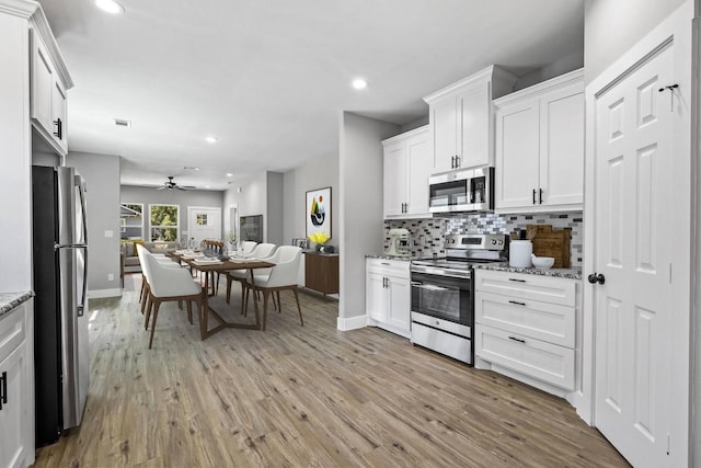 kitchen featuring stainless steel appliances, open floor plan, white cabinets, and light stone counters