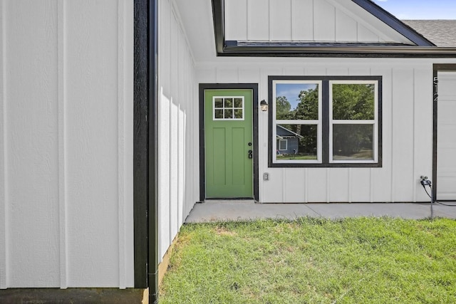 property entrance featuring roof with shingles, board and batten siding, and a yard