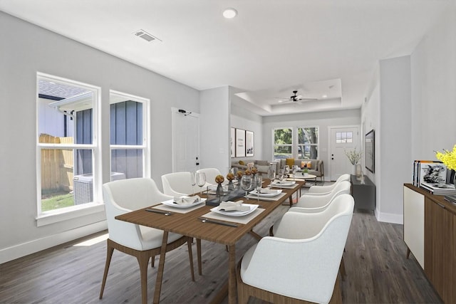 dining space with dark wood-style flooring, a ceiling fan, visible vents, baseboards, and a raised ceiling