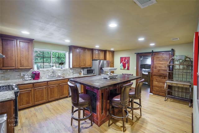 kitchen featuring sink, light hardwood / wood-style flooring, a barn door, appliances with stainless steel finishes, and light stone counters