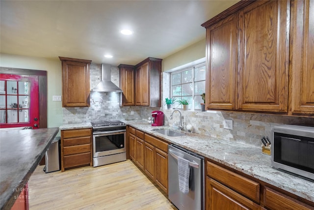 kitchen featuring sink, wall chimney exhaust hood, light hardwood / wood-style floors, decorative backsplash, and appliances with stainless steel finishes