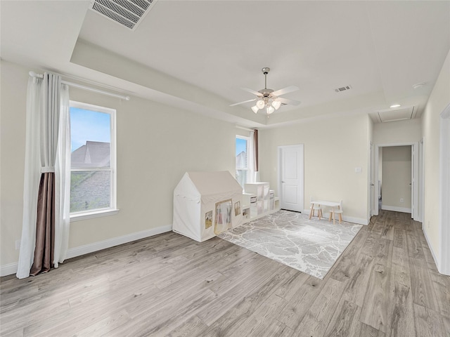 unfurnished bedroom featuring a raised ceiling, visible vents, baseboards, and light wood finished floors