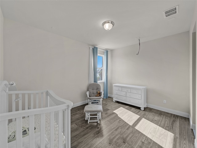 bedroom featuring wood-type flooring and a nursery area