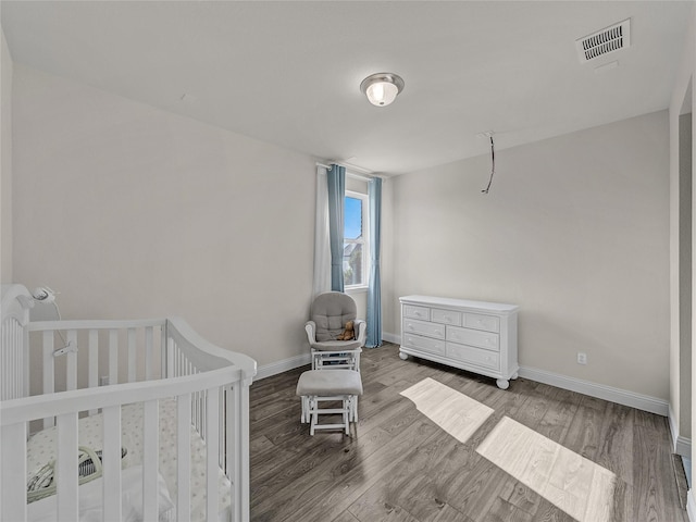 bedroom featuring a nursery area, baseboards, visible vents, and wood finished floors