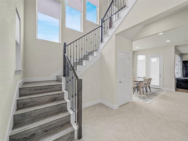 staircase with a high ceiling, recessed lighting, and baseboards