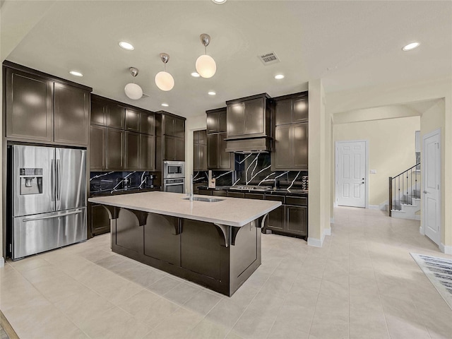 kitchen with visible vents, appliances with stainless steel finishes, decorative light fixtures, a kitchen island with sink, and light countertops