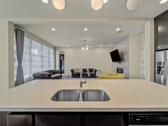 kitchen featuring stainless steel fridge with ice dispenser, open floor plan, a kitchen island with sink, a fireplace, and a sink