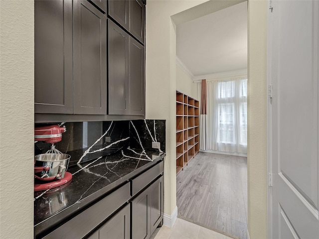 kitchen featuring decorative backsplash, light wood-style floors, ornamental molding, and dark stone countertops