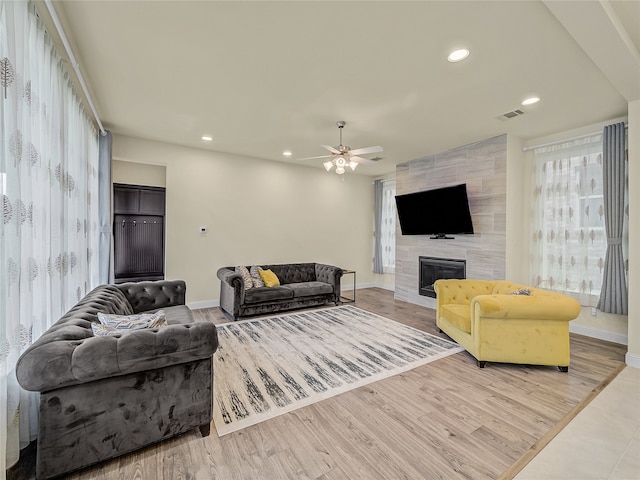 living room featuring tile walls, ceiling fan, light wood-type flooring, and a tile fireplace