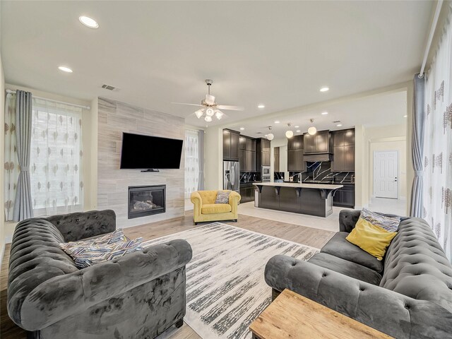 living room featuring a fireplace, ceiling fan, light hardwood / wood-style floors, and tile walls