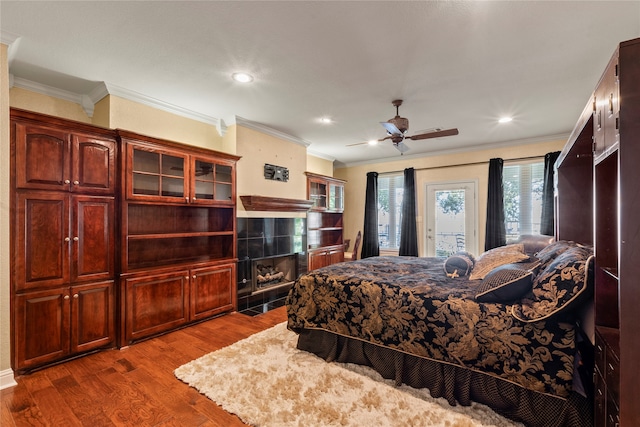 bedroom with ceiling fan, hardwood / wood-style flooring, a tiled fireplace, and crown molding