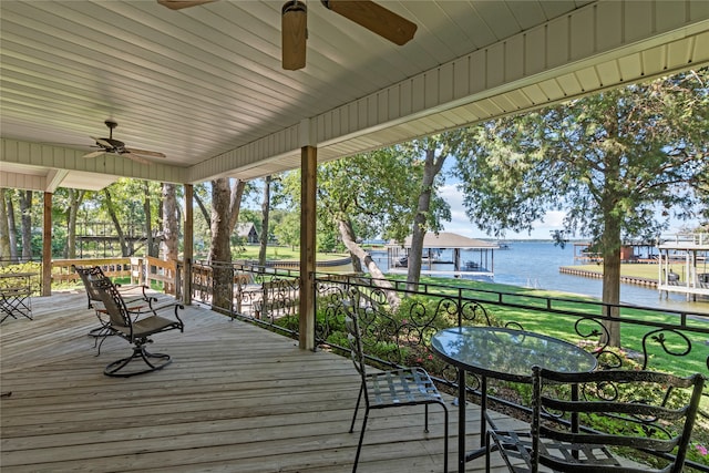 wooden deck with ceiling fan, a boat dock, a lawn, and a water view