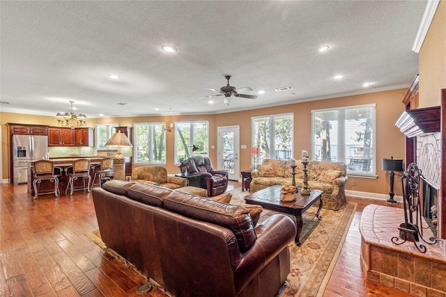 living room with a fireplace, ceiling fan with notable chandelier, ornamental molding, and hardwood / wood-style flooring