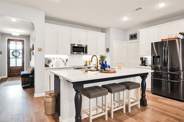 kitchen featuring white cabinetry, stainless steel appliances, light hardwood / wood-style flooring, and an island with sink