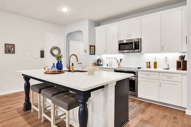 kitchen with appliances with stainless steel finishes, light hardwood / wood-style flooring, a kitchen island with sink, and decorative backsplash