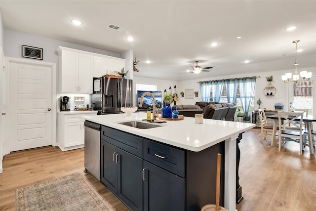 kitchen featuring light hardwood / wood-style flooring, appliances with stainless steel finishes, sink, decorative light fixtures, and a center island with sink