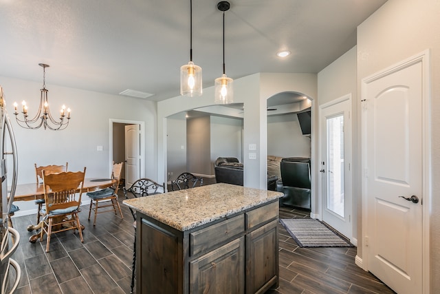 kitchen with light stone countertops, a center island, dark hardwood / wood-style flooring, decorative light fixtures, and dark brown cabinets