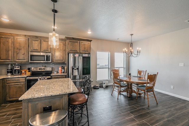 kitchen featuring backsplash, hanging light fixtures, a notable chandelier, a kitchen island, and stainless steel appliances