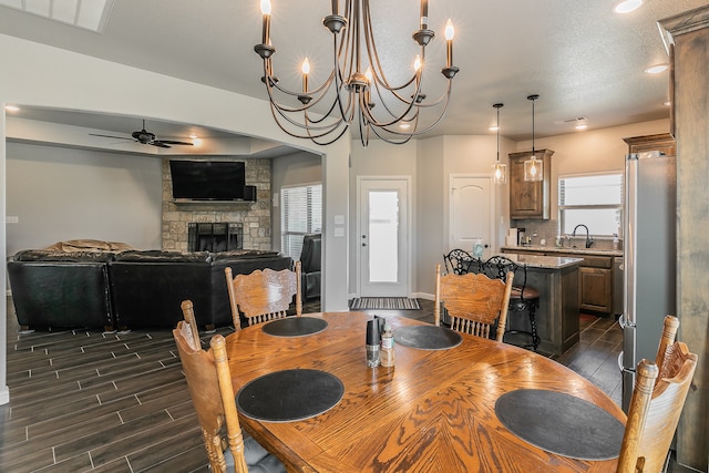 dining area with a fireplace, a textured ceiling, dark hardwood / wood-style flooring, and ceiling fan with notable chandelier