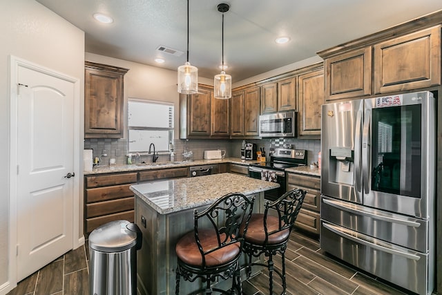 kitchen featuring appliances with stainless steel finishes, light stone counters, sink, a center island, and hanging light fixtures