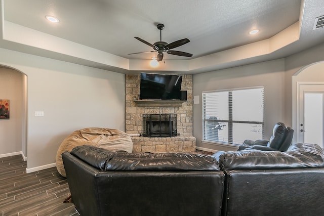 living room with dark hardwood / wood-style flooring, a textured ceiling, a tray ceiling, ceiling fan, and a fireplace