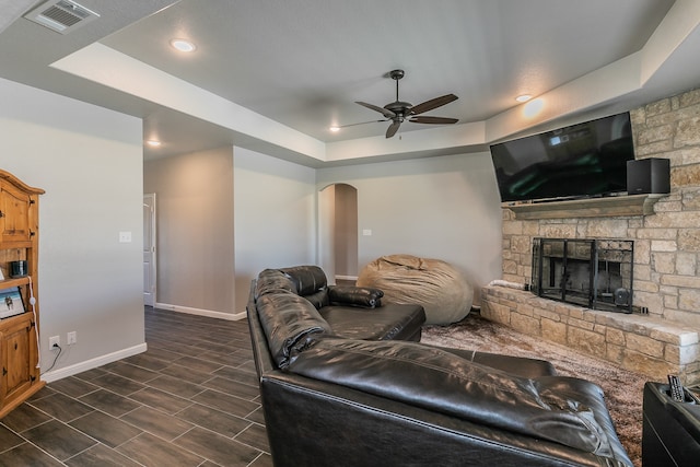 living room with a fireplace, a tray ceiling, ceiling fan, and dark wood-type flooring