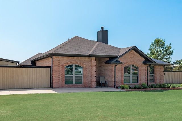 rear view of house featuring a shingled roof, a chimney, a lawn, and brick siding