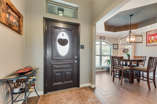 entryway with hardwood / wood-style floors, a raised ceiling, an inviting chandelier, and crown molding